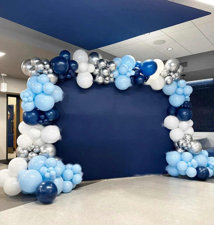 Blue, white and silver balloon arch around a plain navy backdrop